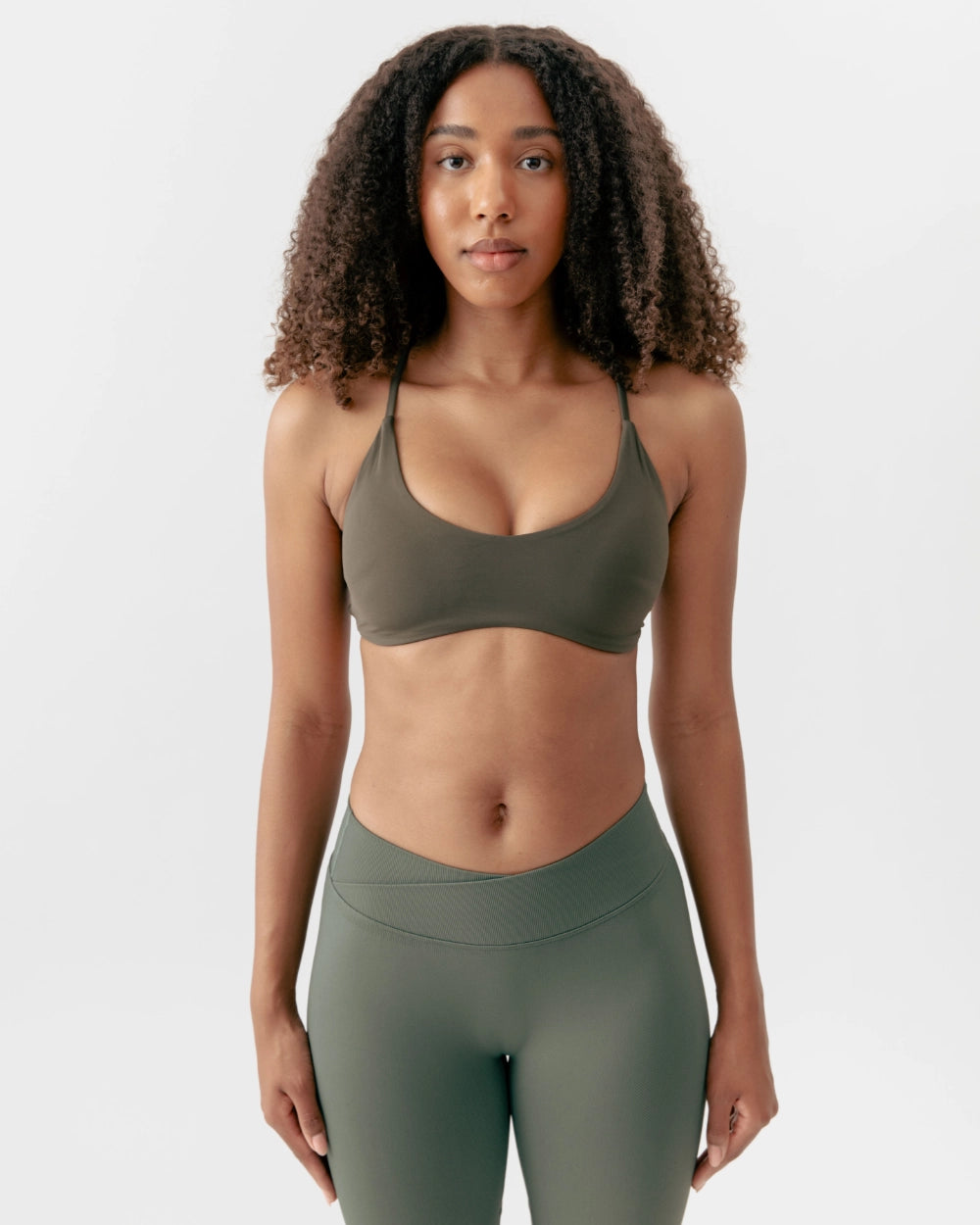 Woman wearing a green sports bra and leggings on a white background