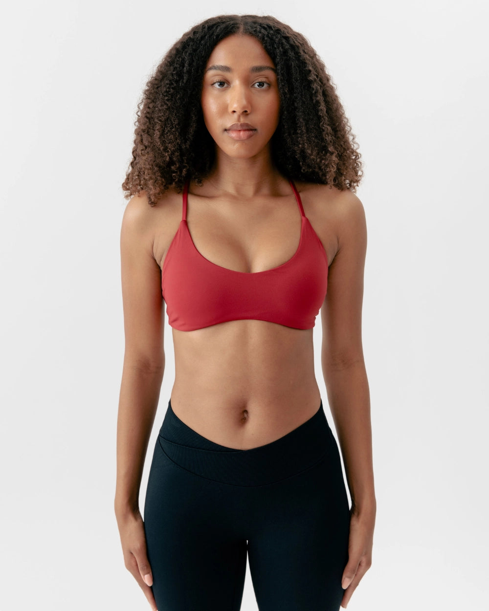 Woman wearing a red sports bra and black leggings on a white background